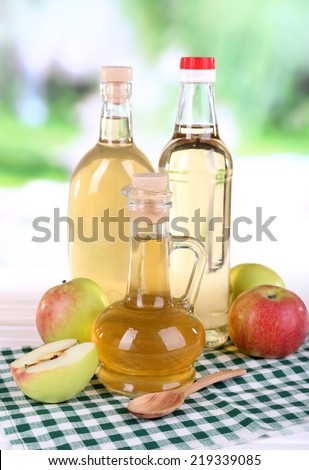 Apple cider vinegar in glass bottles and ripe fresh apples, on wooden table, on nature background