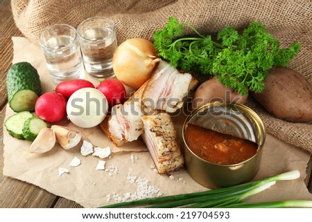 Bacon, fresh vegetables, boiled egg and bread on paper, glasses with vodka on wooden background. Village breakfast concept.