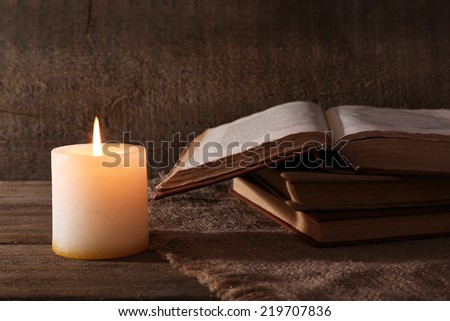 Books and candle on napkin on wooden table on wooden wall background