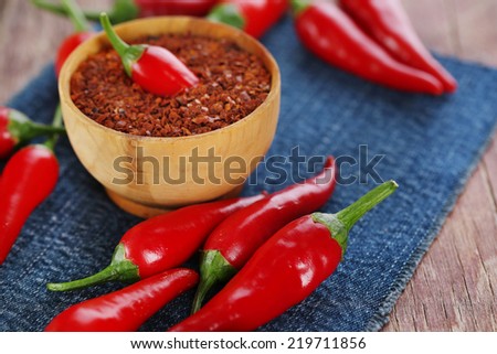 Red hot chili peppers and milled pepper in bowl on color fabric napkin, on wooden background