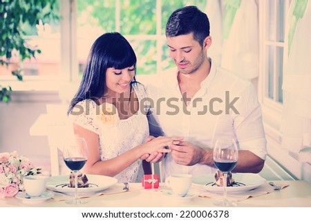 Man proposing and holding up an engagement ring his woman over restaurant table