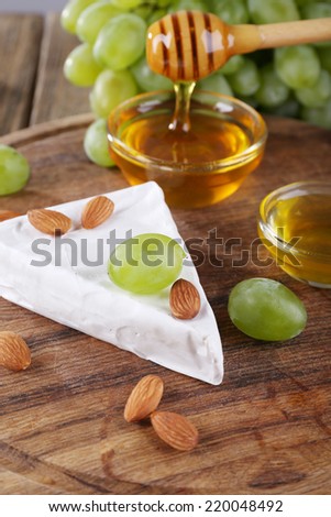 Brie cheese, honey in glass bowl, nuts and grapes on wooden background