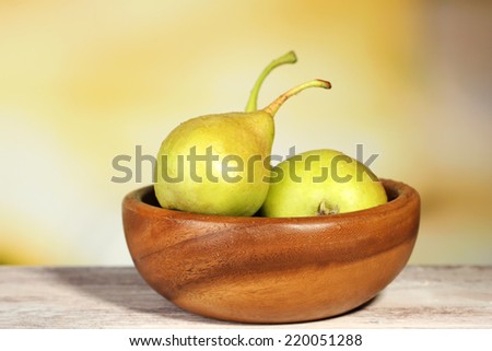 Ripe tasty pears in wooden bowl, on table, on nature background