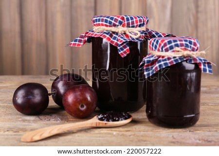 Tasty plum jam in jars and plums on wooden table