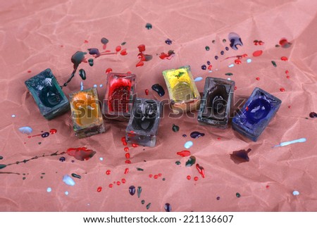 Watercolor paint cubes and spilled paint on brown paper background
