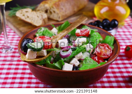 Bowl of Greek salad served with olive oil and bread on fabric background