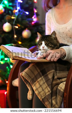Woman and cute cat sitting on rocking chair and read the book, in the front of the Christmas tree