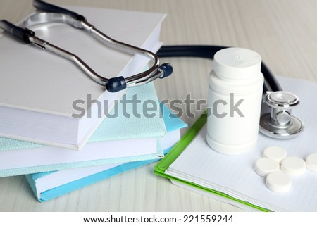Medical stethoscope with books and tablet on wooden table