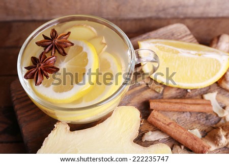Cup of ginger drink with lemon on cutting board on wooden table on wooden wall background