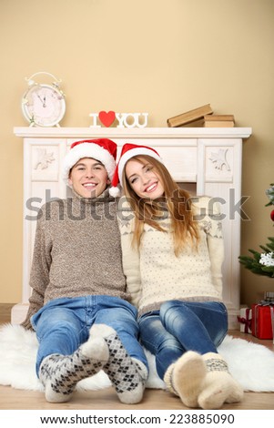 Nice love couple sitting on carpet in front of fireplace. Woman and man celebrating Christmas