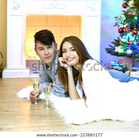 Happy couple having drinks by  fireplace in cozy dark living room on Christmas eve