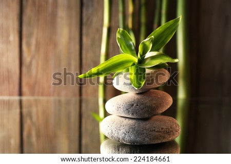 Spa stones and bamboo branches on mirror surface on wooden wall background