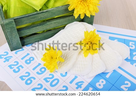 Sanitary pads in dark green box and sanitary pads and yellow flowers on blue calendar background