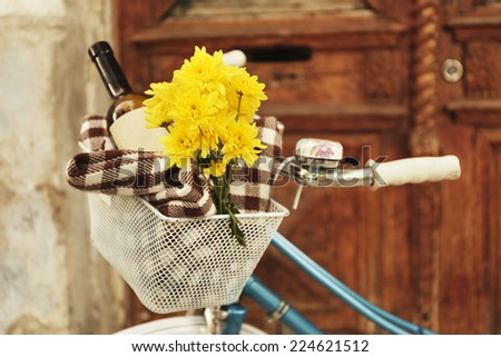 Old bicycle with flowers and checkered blanket in metal basket on brown door background