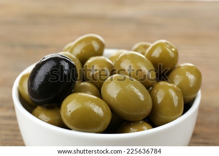Individuality concept. Olive in bowl on wooden table