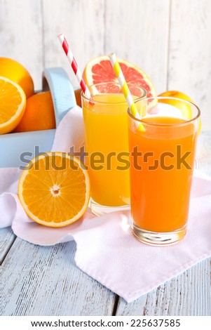 Orange and carrot juice in glasses on napkin and fresh fruits in wooden box on wooden table on wooden wall background