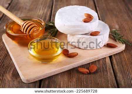 Camembert cheese, honey in glass bowl on cutting board on wooden background