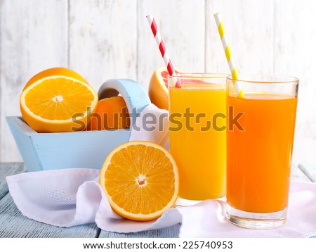Orange and carrot juice in glasses on napkin and fresh fruits in wooden box on wooden table on wooden wall background