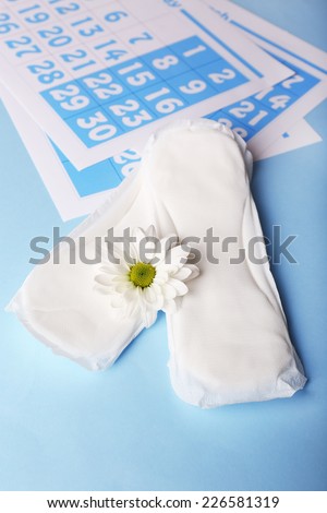 Sanitary pads, calendar and white flower on light blue background