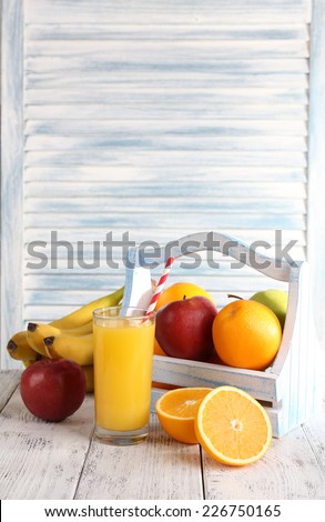 Glass of orange juice and fresh fruits in wooden box on wooden table on wooden wall background