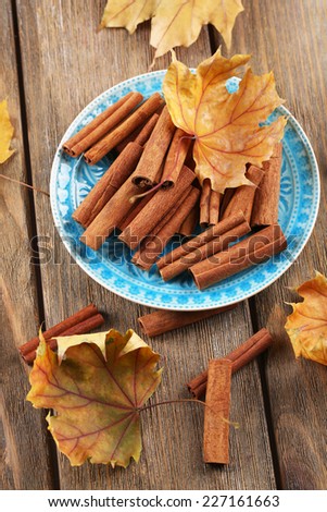 Cinnamon sticks on plate with yellow leaves on wooden background