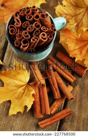 Cinnamon sticks in mug with yellow leaves on wooden background
