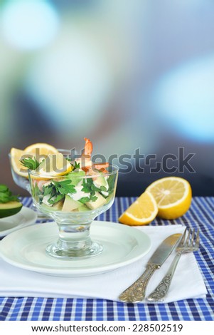 Tasty salads with shrimps and avocado in glass bowl and on plate, on table, on bright background