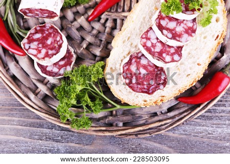 French salami with parsley and chilly pepper on wicker mat on wooden background