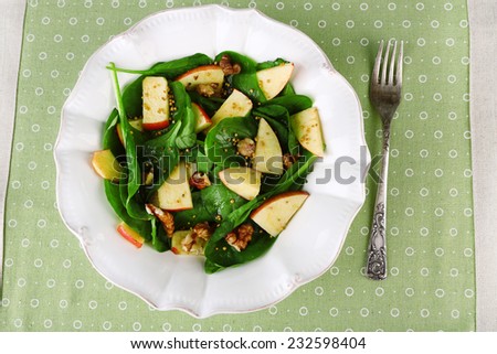 Green salad with spinach, apples, walnuts and cheese on color tablecloth background