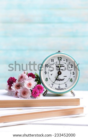 Beautiful flowers with clock and book on table on light blue background