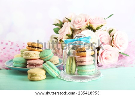Gentle colorful macaroons in glass bell jar and milk glass on color wooden table, on bright background