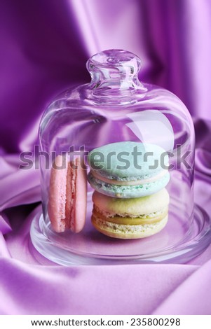 Gentle colorful macaroons in glass bell jar on color fabric background