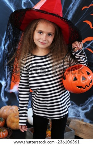 Little girl in hat with pail for candy on Halloween decorations background