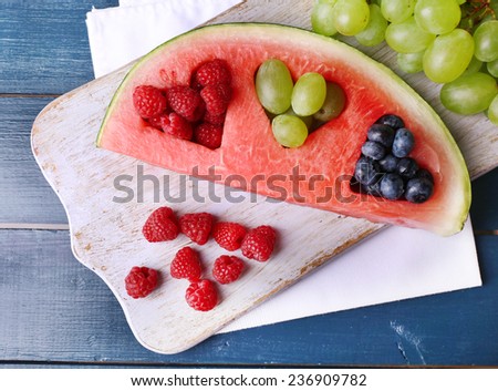 Fresh juicy watermelon slice  with cut out heart shape, filled fresh berries, on cutting board, on color wooden background