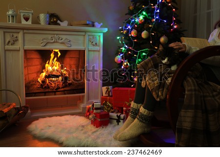 Woman and cute cat sitting on rocking chair and read the book, in the front of the fireplace