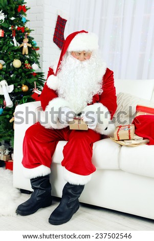 Santa Claus sitting on sofa with  gift boxes near Christmas tree