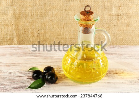 Black olives with green leaves near the oil can on painted wooden table, on burlap background