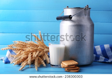 Retro can for milk, milk glass, cookie and sheaf on color wooden background