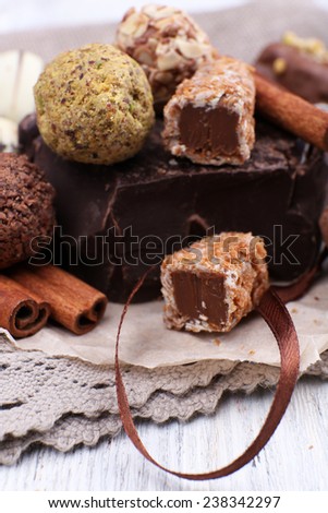 Pile of chunk of chocolate and truffles with cinnamon stick on crumbled paper, grey material and wooden background