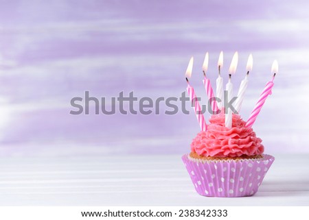 Delicious birthday cupcake on table on light purple background