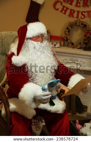 Santa Claus sitting with list of presents in comfortable chair near fireplace at home