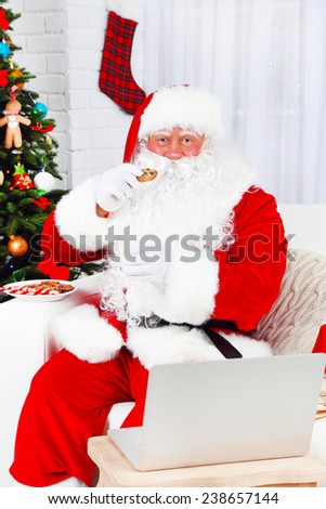 Modern Santa Claus sitting on sofa and using computer