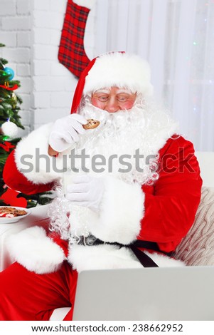 Modern Santa Claus sitting on sofa and using computer