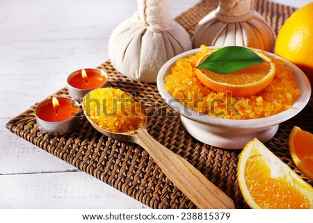 Accessories for massage therapy with candle light, spoon and bowl of bath salt on wicker mat, on color wooden background