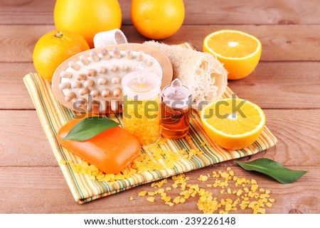 Spa still life with oranges, bottles of bath salt and oil, and bar of soap on striped napkin on wooden background