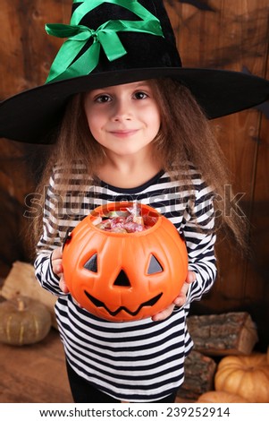Little witch girl in hat asks candy on Halloween decorations background