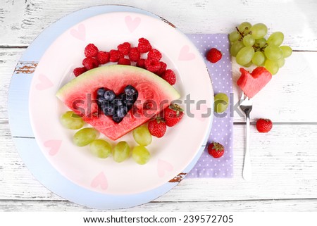 Fresh juicy watermelon slice  with cut out heart shape, filled fresh berries, on plate, on wooden background