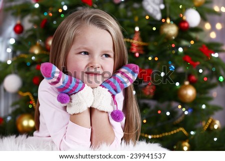 Little girl with mittens lying on fur carpet on Christmas tree background