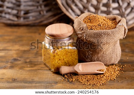 Mustard seeds in bag and Dijon mustard in glass jar on wooden background