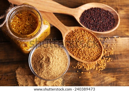 Mustard seeds, powder and sauce in glass jar, bowl and wooden spoons on wooden background